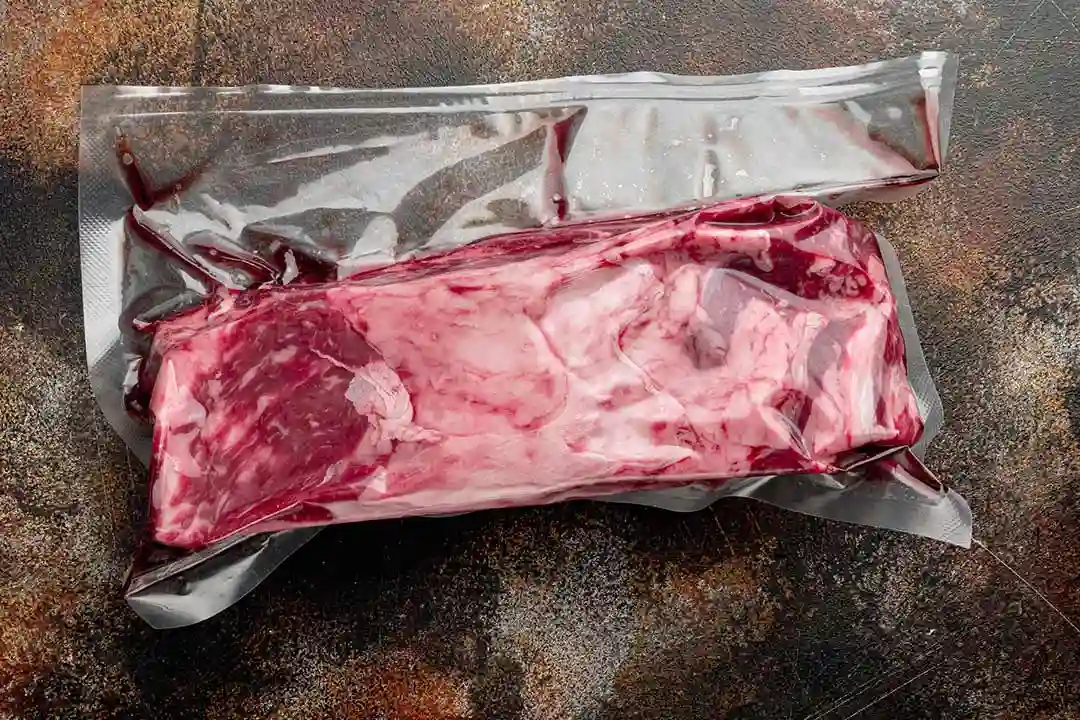 Carnicero utilizando una envasadora al vac&iacute;o de campana profesional de acero inoxidable para conservar cortes de carne fresca.
