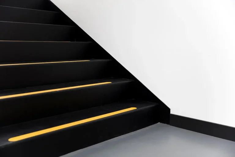 T&eacute;cnico en prevenci&oacute;n instalando cintas antideslizantes escaleras de color amarillo y negro en una rampa industrial met&aacute;lica.