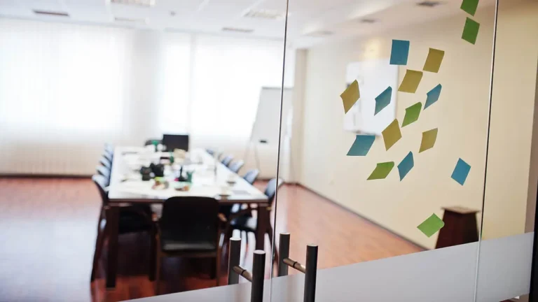 Sala de reuniones en oficina moderna con pizarra magn&eacute;tica y placa de puerta.