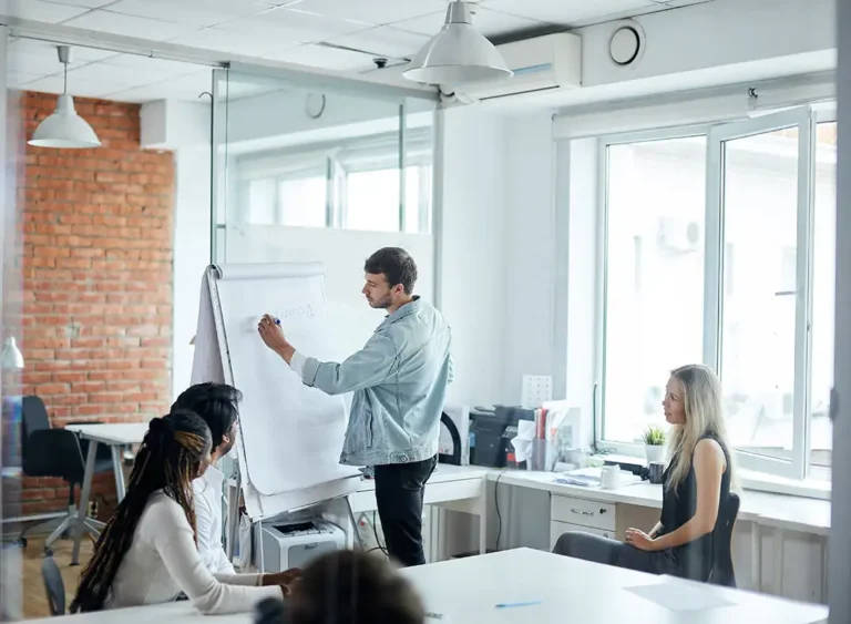 Equipo de profesionales trabajando juntos frente a una pizarra blanca en la oficina, anotando ideas con rotuladores.